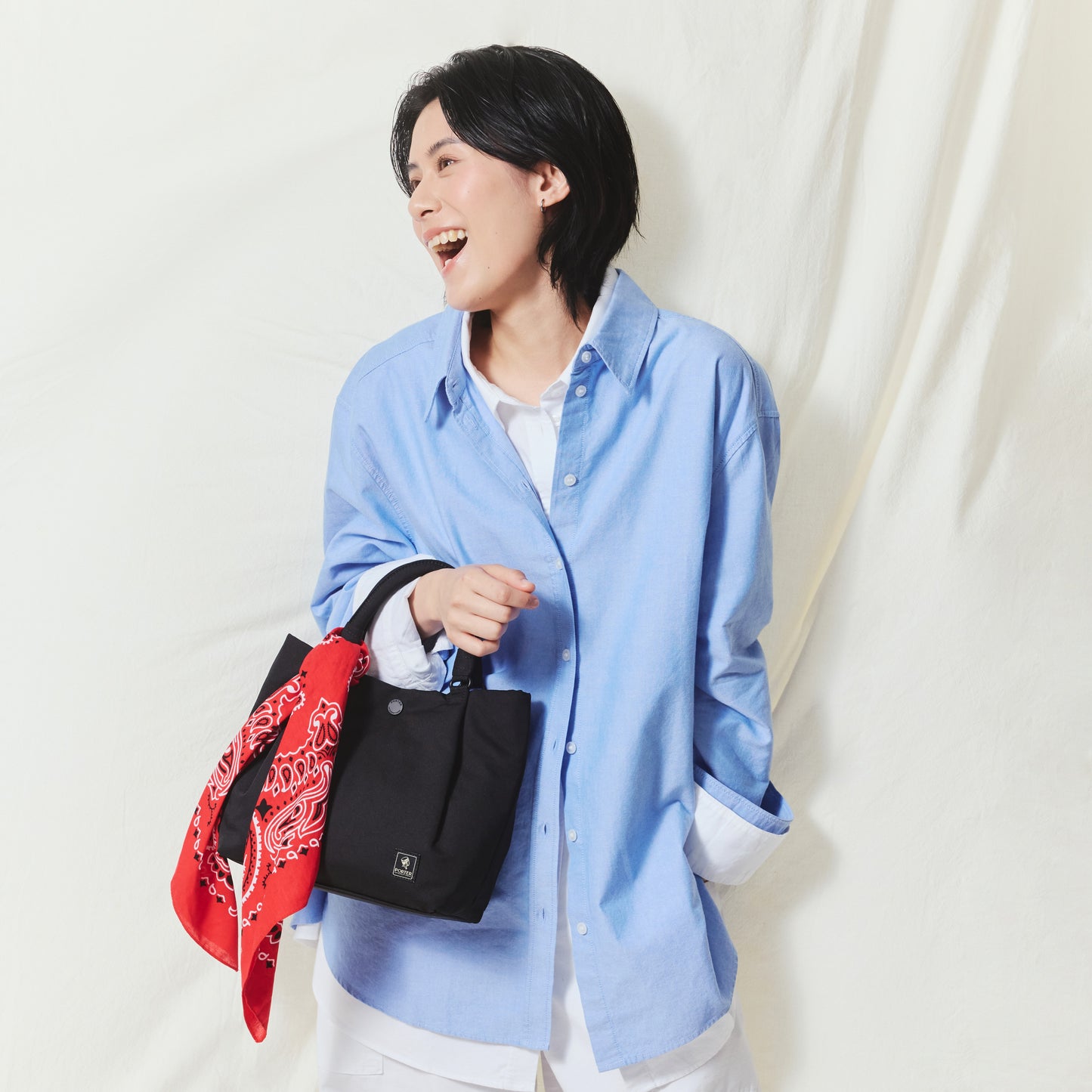 Model carrying the PORTER INTERNATIONAL Cush Handbag (M) 'Black', a lightweight everyday handbag with a minimalist design and spacious interior.