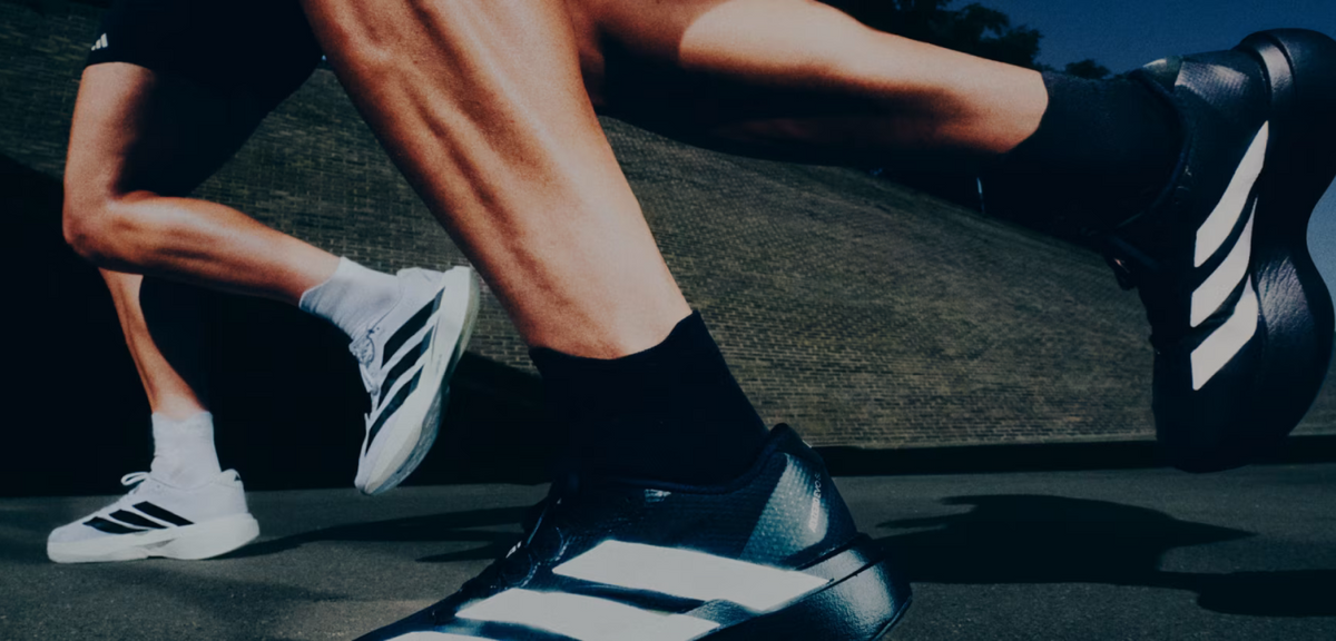 Close-up of adidas Performance ADIZERO EVO SL EXO Black White Silver running shoes worn by a runner on an outdoor paved surface, featuring lightweight LIGHTSTRIKE PRO cushioning.
